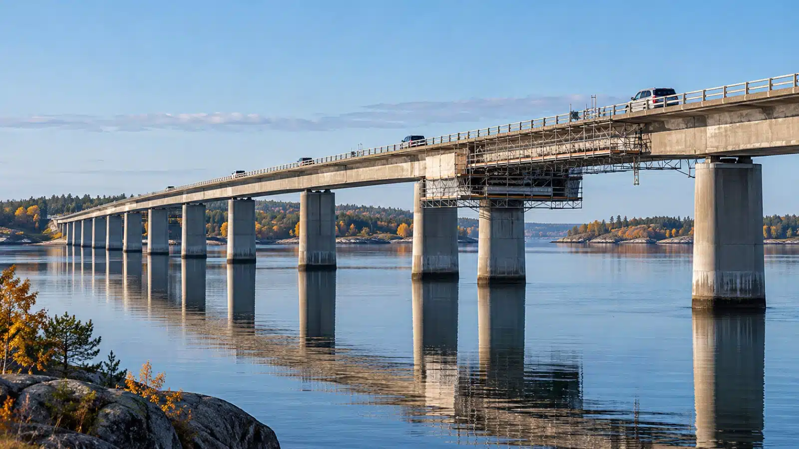 AI-genererad bild av en lång betongbro med många pelare över blankt vatten en klar höstdag